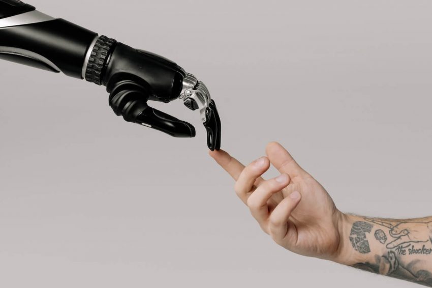 An image depicting a robotic hand and a human hand in a reminiscent pose of Michelangelo's "Creation of Adam," symbolizing the intersection of AI tech and humanity.